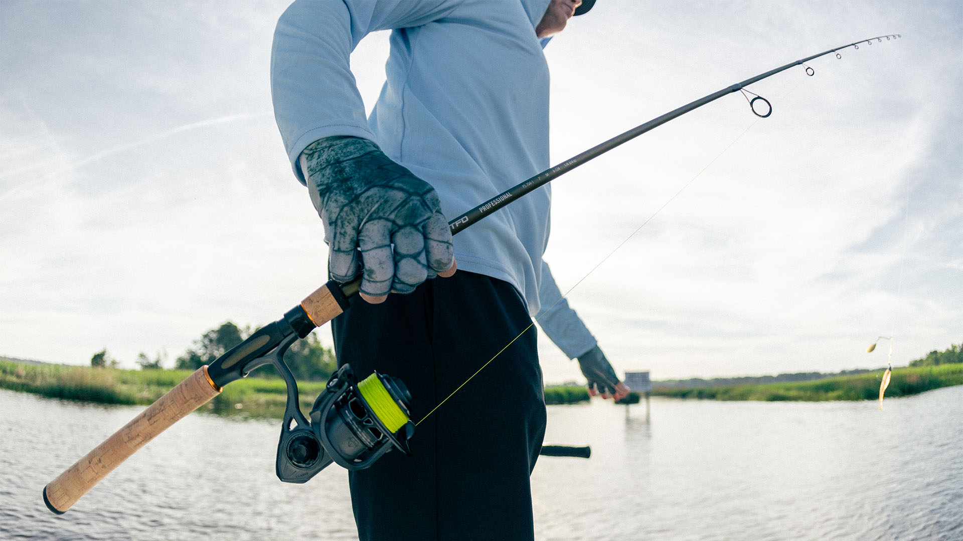 Angler holding a TFO Professional Series spinning rod and reel over shallow inshore water on a calm day, showcasing a versatile setup for freshwater and inshore fishing.